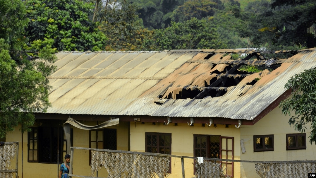 FILE - A woman stands outside the damaged roof of a school's dormitory, after it was set to fire overnight in Bafut, in the northwest English-speaking region of Cameroon, Nov. 15, 2017.
