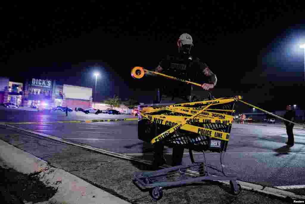 A law enforcement officer attaches a crime scene tape to a shopping cart after a shooting at a mall in the Indianapolis suburb of Greenwood, Indiana, July 17, 2022. 