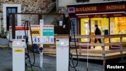 FILE - A woman comes out of a bakery behind fuel pumps at gas station in the village of Langon near Rennes, France, Oct. 21, 2021. 