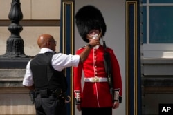 FILE - A police officer givers water to a British soldier wearing a traditional bearskin hat, on guard duty outside Buckingham Palace, during hot weather in London, July 18, 2022.