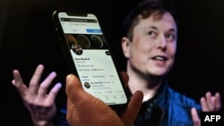 FILE - In this illustration, a phone displaying the Twitter account of Elon Musk is held up in front of a photo of him, in Washington, D.C., April 14, 2022.