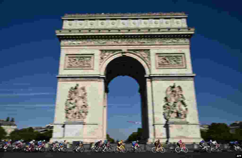 Jumbo-Visma team&#39;s Danish rider Jonas Vingegaard wearing the overall leader&#39;s yellow jersey (C) cycles with the pack of riders past the Arc de Triomphe during the 21st and final stage of the 109th edition of the Tour de France cycling race, 115,6 km between&nbsp;La Defense Arena in Nanterre, outside Paris, and the Champs-Elysees in Paris, France.