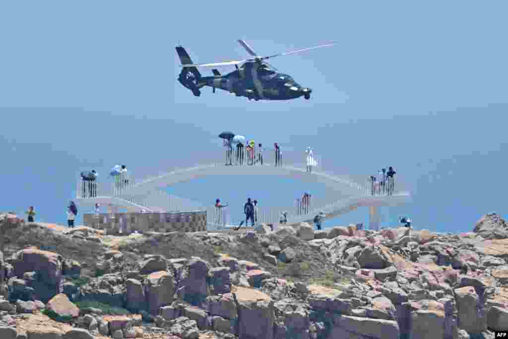 Tourists look on as a Chinese military helicopter flies past Pingtan island, one of mainland China&#39;s closest point from Taiwan, in Fujian province, ahead of massive military drills off Taiwan following U.S. House Speaker Nancy Pelosi&#39;s visit to the self-ruled island.