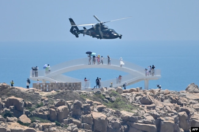 Tourists look on as a Chinese military helicopter flies past Pingtan island, one of mainland China's closest point from Taiwan, in Fujian province, Aug. 4, 2022, ahead of massive military exercises off Taiwan. (Photo by Hector RETAMAL / AFP)