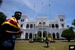 Para pengunjuk rasa mengibarkan bendera nasional Sri Lanka, bersiap mengosongkan gedung kantor Perdana Menteri Ranil Wickremesinghe bersama pengunjuk rasa lainnya di Kolombo, Sri Lanka, Kamis, 14 Juli 2022. (AP Photo/Eranga Jayawardena)