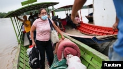 Migrantes venezolanos llegan en canoas a orillas del río Arauca del lado colombiano portando sus pertenencias tras huir de su país por operativos militares, según la agencia colombiana de migración, en Arauquita, el 27 de marzo de 2021.