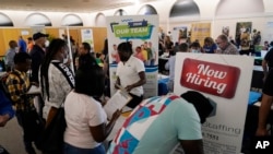 FILE - Job applicants fill out forms with CSC Global, left, and Skilled Staffing, right, at the 305 Second Chance Job & Resource Expo, June 10, 2022, in Miami. 