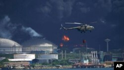 A helicopter carrying water flies over the Matanzas Supertanker Base, as firefighters try to quell the blaze which began during a thunderstorm the night before, in Matazanas, Cuba, Aug. 6, 2022.