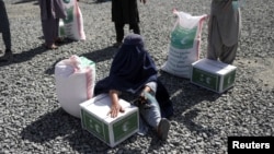 FILE - An Afghan woman waits to receive a food package distributed by a Saudi Arabia humanitarian aid group at a distribution center in Kabul, Afghanistan, April 25, 2022. 