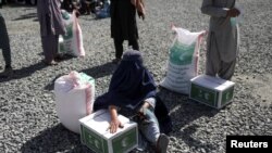 FILE - An Afghan woman waits to receive a food package distributed by a Saudi Arabia humanitarian aid group at a distribution center in Kabul, Afghanistan, April 25, 2022. 