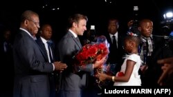 Une jeune fille offre des fleurs au président français Emmanuel Macron à son arrivée à Yaoundé, où il a été accueilli par le Premier ministre Joseph Dion Ngute (à g.), le 25 juillet 2022.