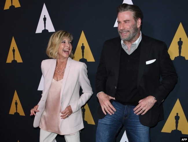 FILE - Actors Olivia Newton-John and John Travolta dance on the red carpet as they arrive for the 40th anniversary celebration of the movie "Grease" at the Academy of Motion Picture Arts and Sciences in Beverly Hills, California, Aug. 15, 2018.