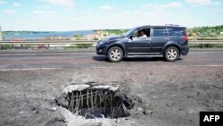 a car moving past a crater on Kherson's Antonovsky bridge across the Dnipro river caused by a Ukrainian rocket strike