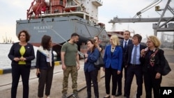 En esta foto proporcionada por la Oficina de Prensa Presidencial de Ucrania, el presidente de Ucrania, Volodymyr Zelenskyy, en el centro, rodeado de embajadores de diferentes países y funcionarios de la ONU, visita un puerto en Chornomork durante la carga de granos en un barco turco, al fondo, cerca de Odesa, Ucrania. Viernes, 29 de julio de 2022. (Oficina de Prensa Presidencial de Ucrania vía AP)