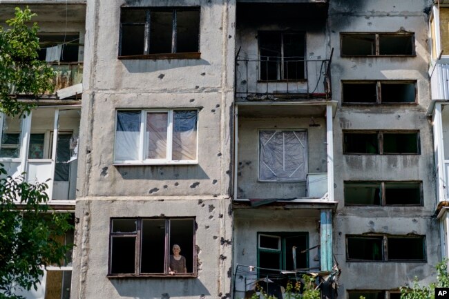 Ida Svystunova, 89, looks out the damaged room adjoining her apartment from a May rocket attack in Sloviansk, Donetsk region, eastern Ukraine, Sunday, Aug. 7, 2022. (AP Photo/David Goldman)