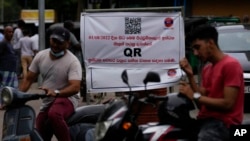 Motorists wait next to a banner that says only those vehicles with QR codes will be given fuel at a fuel station in Colombo, Sri Lanka, Aug. 1, 2022. 