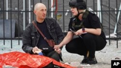 A police officer, right, comforts a man as he holds the hand of a relative killed in Russian shelling in Kharkiv, Ukraine, July 20, 2022.