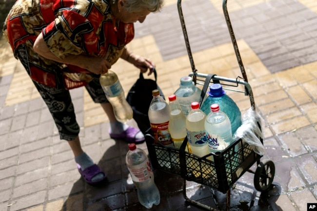 Lyubov Mahlii, 76, packs a crate with water bottles she filled up at a public tank to take back to her apartment in Sloviansk, Donetsk region, eastern Ukraine, Saturday, Aug. 6, 2022. " (AP Photo/David Goldman)