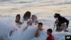 Sejumlah warga Palestina tampak bermain di pantai untuk mendinginkan badan mereka di tengah cuaca panas yang melanda pada 22 Juli 2022. Pantai tersebut terletak di Beit Lahia, sebelah utara Jalur Gaza. (Foto: AP/Hatem Moussa)