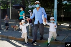 A man leads two children wearing masks to cross the road in Beijing, July 17, 2022.
