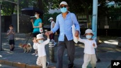 A man leads two children wearing masks to cross the road in Beijing, July 17, 2022.