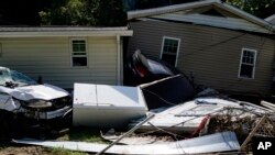 Homes lean against each other after massive flooding swept them away on Thursday, Aug. 4, 2022, in Chavies, Kentucky. Between the black car and couch is where Patricia Collins was pinned by rushing water until the car's flashing tail light alerted rescuer