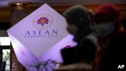 Two women wearing face mask walks in front of the ASEAN logo at a hotel where the 55th ASEAN Foreign Ministers' Meeting (55th AMM) is taking place in Phnom Penh, Cambodia, Tuesday, Aug. 2, 2022.