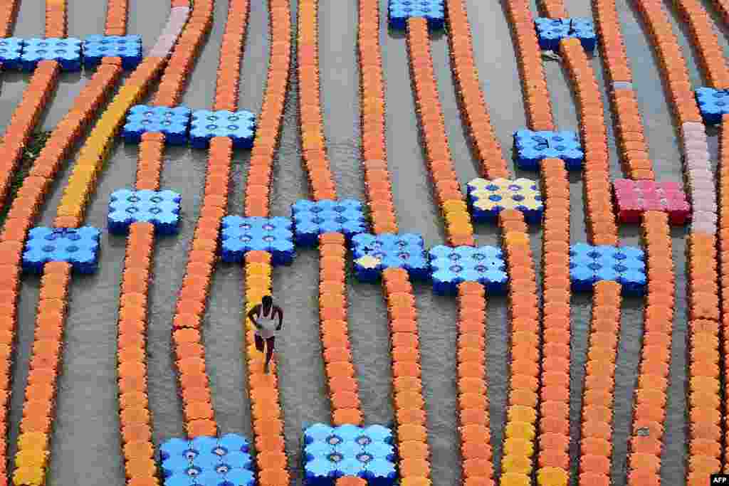 A boatman walks on a floating dock made of plastic cubes along the flooded banks of River Ganges after a rise in the water level due to heavy rains in Allahabad, India, July 30, 2022.