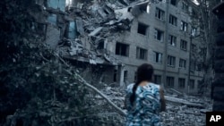 在乌克兰尼古拉耶夫夜间遭到俄军炮击后，一位乌克兰女士走过一座居民楼废墟。(2022年8月2日)