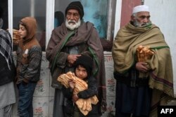 FILE - People stand as they receive free bread distributed as part of the Save Afghans From Hunger campaign in front of a bakery in Kabul, Jan. 18, 2022.