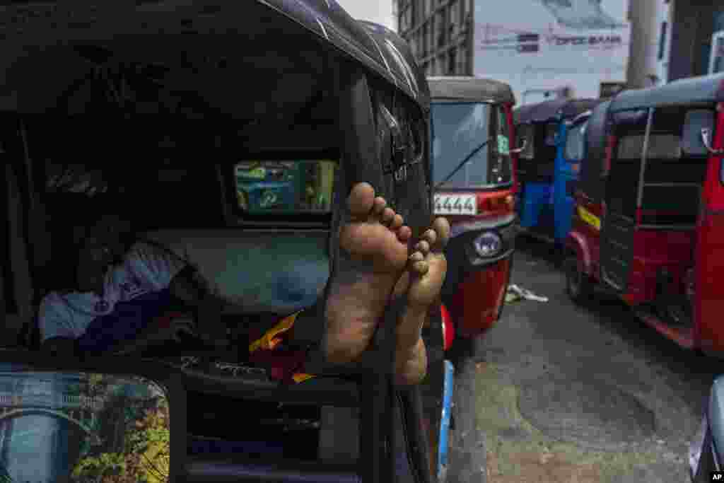 A driver of an autorickshaw sleeps inside his rickshaw while waiting in a queue to buy petrol at a fuel station in Colombo, Sri Lanka.