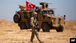 FILE - A U.S. soldier walks past a Turkish armored vehicle during the first joint ground patrol of American and Turkish forces in the so-called "safe zone" on the Syrian side of the border with Turkey, near Tal Abyad, Syria, Sept. 8, 2019.