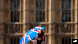 Una madre protege a su bebé del sol con un paraguas el martes 19 de julio de 2022, mientras camina por el puente de Westminster en Londres. (AP Foto/Frank Augstein)