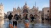 FILE - People cross St Mark's Square flooded by sea tide, in Venice, Italy, Dec. 4, 2021. The water reached 99 centimeters above sea level and the lowest parts of town went underwater.