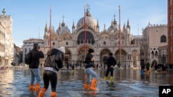 FILE - People cross St Mark's Square flooded by sea tide, in Venice, Italy, Dec. 4, 2021. The water reached 99 centimeters above sea level and the lowest parts of town went underwater.