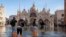 FILE - People cross St Mark's Square flooded by sea tide, in Venice, Italy, Dec. 4, 2021. The water reached 99 centimeters above sea level and the lowest parts of town went underwater.