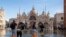 Sejumlah orang tampak berjalan melintasi alun-alun St Mark di Venesia, Italia, yang digenangi oleh banjir rob pada 4 Desember 2021. (Foto: AP/Luigi Costantini)