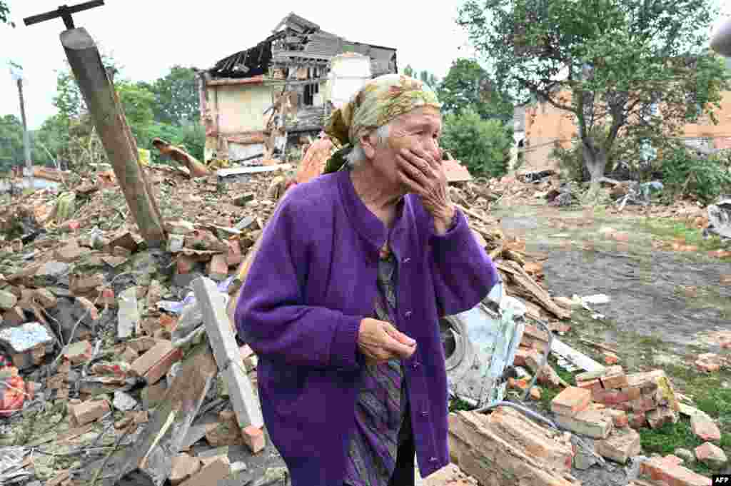 A local resident, Raisa Kuval, 82, reacts next to a damaged building partially destroyed after a shelling in the city of Chuguiv, east of Kharkiv, Ukraine, July 16, 2022.