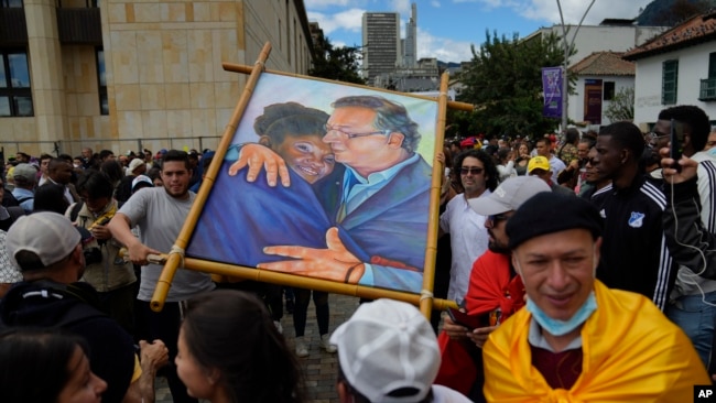 Partidarios del nuevo presidente Gustavo Petro exhiben una pintura de él con la nueva vicepresidenta Francia Márquez mientras esperan la ceremonia de juramentación en la plaza de Bolívar en Bogotá, Colombia, el domingo 7 de agosto de 2022. (Foto AP/Ariana Cubillos )