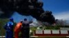 Oil workers watch smoke from the Matanzas Supertanker Base as firefighters work to quell a blaze which began during a thunderstorm the night before, in Matazanas, Cuba, Aug. 6, 2022.