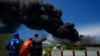 Pekerja menyaksikan asap dari Pangkalan Supertanker Matanzas saat petugas pemadam kebakaran bekerja untuk memadamkan api di Matazanas, Kuba, 6 Agustus 2022. (Foto: AP)