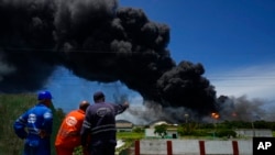 Pekerja menyaksikan asap dari Pangkalan Supertanker Matanzas saat petugas pemadam kebakaran bekerja untuk memadamkan api di Matazanas, Kuba, 6 Agustus 2022. (Foto: AP)