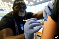 FILE - DeMarcus Hicks, a recent graduate of nursing school who is working as a contractor with the Federal Emergency Management Agency, gives a person a Pfizer COVID-19 vaccine booster shot, Dec. 20, 2021.