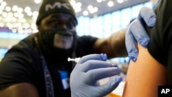 FILE - DeMarcus Hicks, a recent graduate of nursing school who is working as a contractor with the Federal Emergency Management Agency, gives a person a Pfizer COVID-19 vaccine booster shot, Dec. 20, 2021.