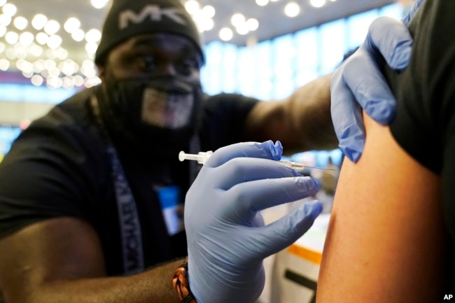 FILE - DeMarcus Hicks, a recent graduate of nursing school who is working as a contractor with the Federal Emergency Management Agency, gives a person a Pfizer COVID-19 vaccine booster shot, Dec. 20, 2021.