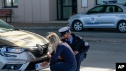 FILE - A Kosovo police officer helps a Serb driver place stickers covering state symbols on her car's license plates, at Merdare border crossing, Oct. 4, 2021.