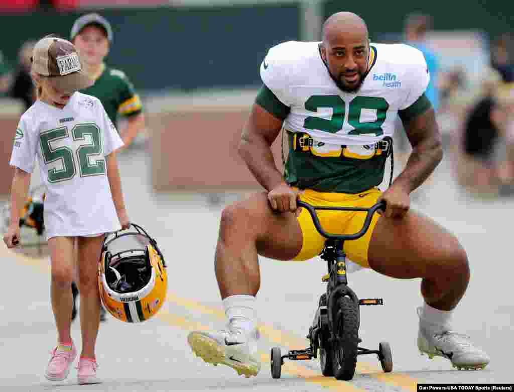 A young fan watches as Green Bay Packers running back AJ Dillon (28) tries his best to ride her bicycle to training camp, August 1, 2022, at Ray Nitschke Field in Green Bay, Wisconsin.