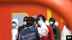 Una trabajadora de la salud toma la temperatura de los migrantes que desembarcan tras un rescate en la isla de Lampedusa, Italia, el 11 de mayo de 2021.
