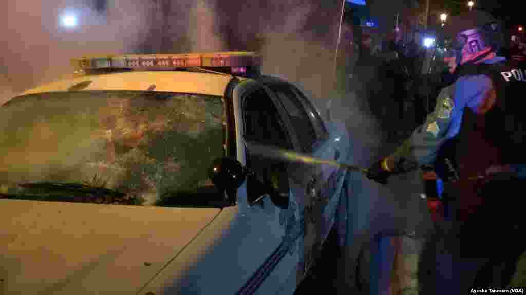 Seorang petugas polisi berupaya memadamkan api di dalam mobil polisi, di luar Balai Kota Ferguson, Missouri, 25 November 2014 .