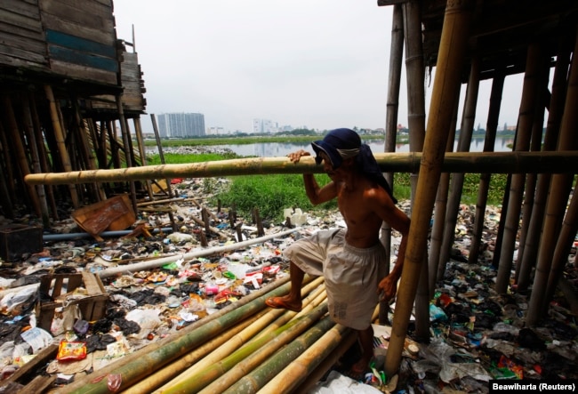 Ujang Ahmad membawa tiang bambu untuk memperbaiki rumahnya yang rusak di kawasan kumuh dekat waduk Pluit, Jakarta, 22 Februari 2012. Presiden Joko Widodo meminta kemiskinan dientaskan pada 2024.(Foto: REUTERS/Beawiharta)